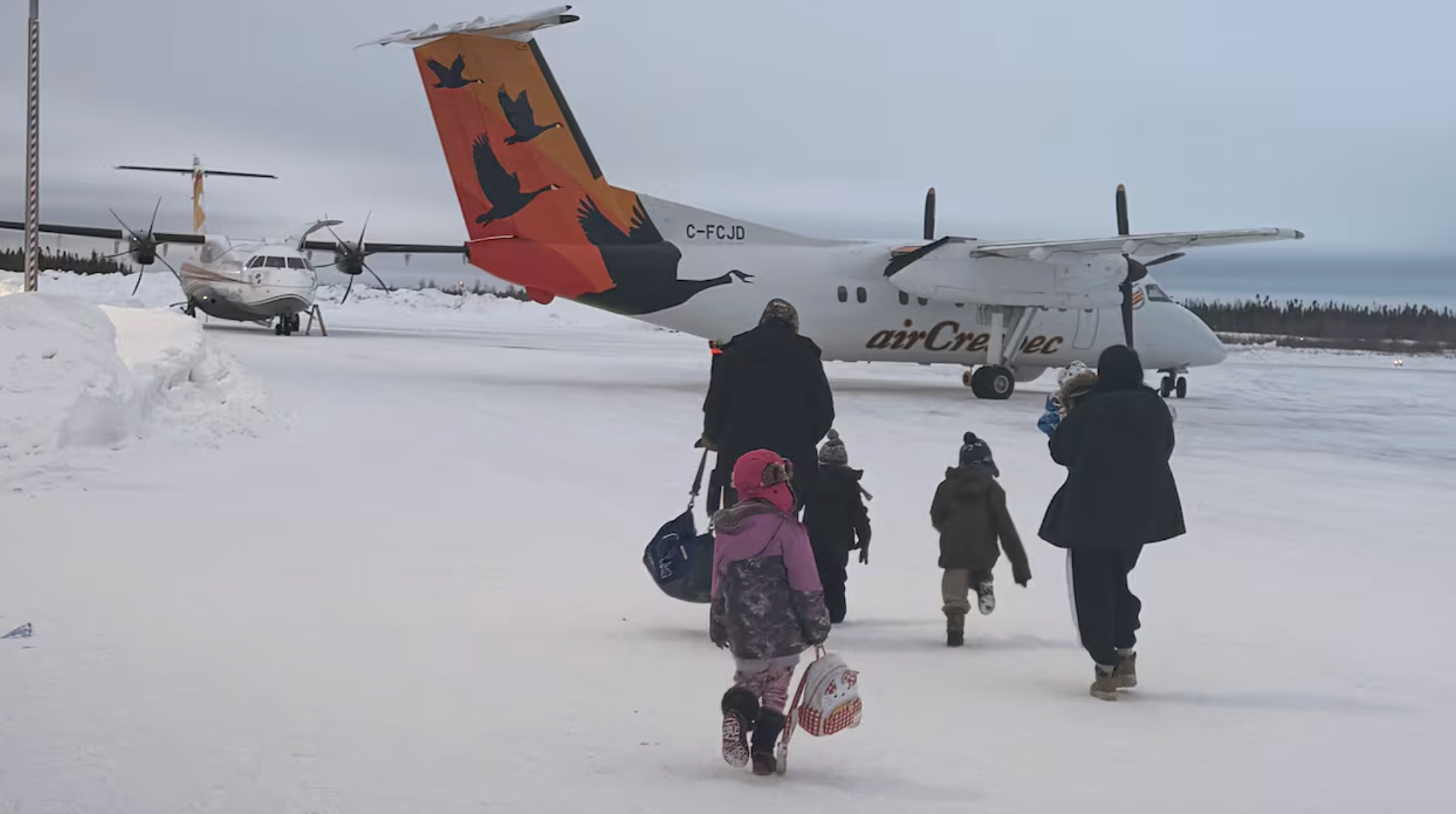 A family walks toward a small plane on a snowy tarmac.